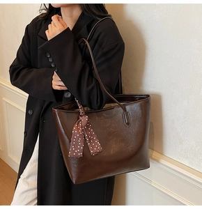 Detail of dark brown tote bag with glossy finish and polka dot silk scarf handle decor