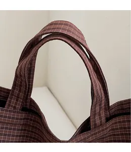 Détail des doubles poignées renforcées sur un sac cabas marron foncé à carreaux