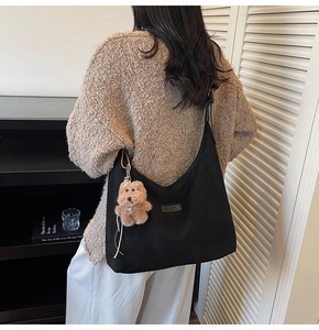 Detail of a black nylon hobo bag with a leather logo patch and a brown plush bear charm
