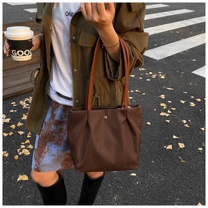 Detail of dark brown tote bag with silk texture, pleats, and gold hardware in autumn scene