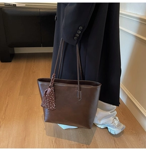 Detail of deep brown leather tote bag with a polka dot scarf accessory on black coat