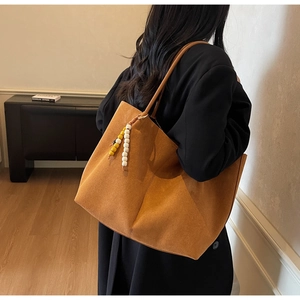 Detail of soft brown suede tote bag featuring a decorative beaded charm and slim shoulder strap