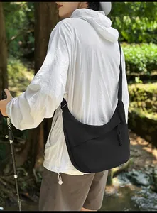 Outdoor model shot showing the back view of a black crescent nylon crossbody bag with rope zip
