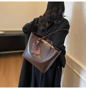 Detail of a large dark brown leather tote bag with a polka dot silk scarf on the shoulder