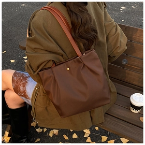 Detail of coffee brown nylon tote bag featuring gold rivet on autumn leaves background