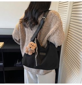 Detail of black suede tote bag with leather strap and cute brown plush bear charm