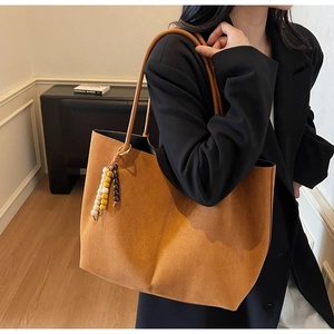 Detail of caramel suede tote bag with colorful beaded tassel on black blazer background