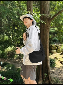 Black nylon crossbody bag with decorative drawstring shown in forest hiking scenario