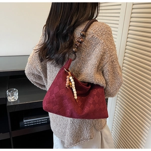 Detail of burgundy suede shoulder bag with diamond quilting and decorative beaded handle