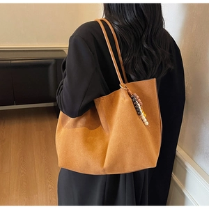 Detail view of large tan suede tote bag with stylish beaded tassel and long shoulder strap