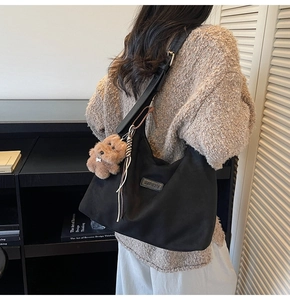 Detail of a black oversized hobo bag with a brown teddy bear charm and brand logo label