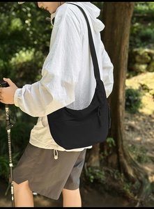 Detail of black large capacity crescent crossbody bag with woven decorative zipper pull