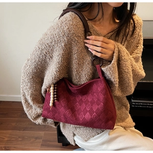Detail of burgundy quilted tote bag with wooden beads and rope strap on model