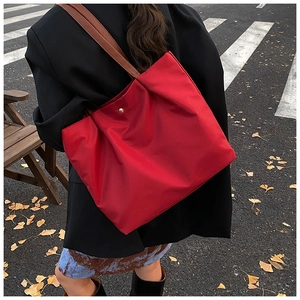 Close-up of red tote bag with brown leather straps and gold magnetic snap closure details