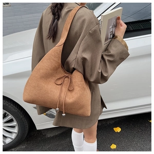 Close-up of brown suede hobo bag with bow detail and metal ball pendant on shoulder