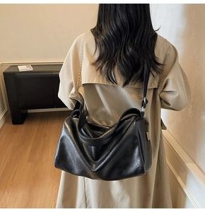 Close-up of minimalist black leather tote bag with metal plaque on the side strap