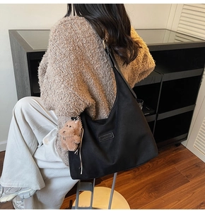 Detailed view of black hobo tote bag worn by model featuring a plush bear charm