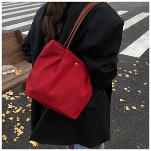 Red large tote bag on shoulder over black blazer against autumn street background