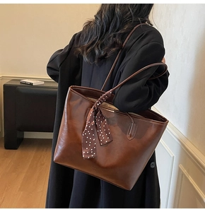 Close-up of brown faux leather tote bag with decorative polka dot scarf on handle