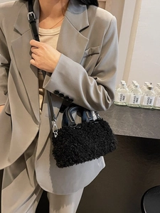Furry black lamb wool crossbody bag with leather handles shown on a model in a gray suit