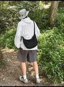 Detail of a black nylon crescent crossbody bag in an outdoor forest hiking setting