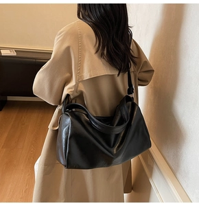 Rear view of a minimalist black large capacity leather tote bag worn by a model in a room