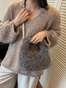 Grey curly faux fur handbag with shoulder strap shown in a cozy indoor lifestyle setting