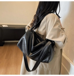 Detail of a large black PU leather tote bag with stylish drape pleats shown on a model