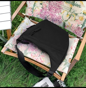 Detail of a black nylon crescent shoulder bag on a floral chair in a natural setting