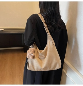 Detail view of khaki hobo bag with plush bear charm and brand logo on premium faux suede