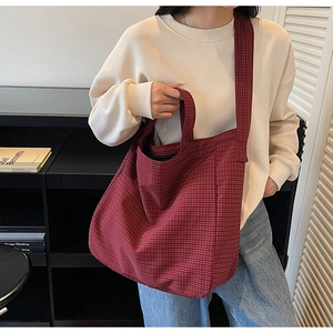 Detail of red plaid canvas tote bag with dual handles in a minimalist interior setting