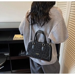 Detail of a chic black leopard print crossbody bag worn by a model in a cozy indoor setting