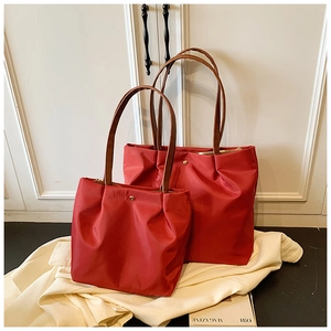 Detail of red waterproof nylon tote bags in two sizes with leather straps and gold snap buttons