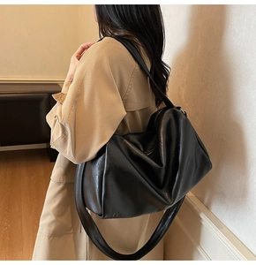 Side view of a large black faux leather tote bag worn by a model in a warm interior