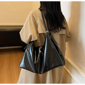 Chic black hobo bag in polished leather finish worn over the shoulder with a trench coat