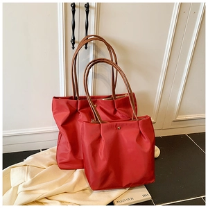 Macro detail of red nylon tote bags in two sizes with brown leather handles and rivets