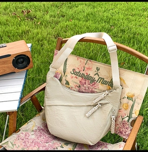 Detail of beige crescent crossbody bag with utility pockets and woven zipper pulls