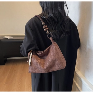 Detail of brown suede shoulder bag featuring embossed patterns and decorative wooden beads