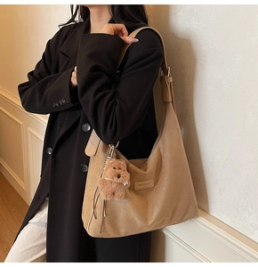 Detail of khaki suede hobo bag with teddy bear pendant worn by model in black blazer