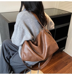 Detail of a large brown matte leather tote bag with soft texture and wide shoulder strap