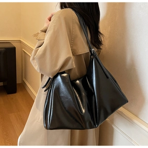 Detail of glossy black leather tote bag with adjustable strap worn on woman's shoulder