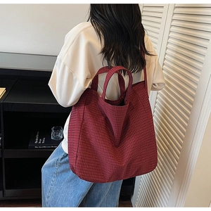 Detail showing red checkered canvas tote bag with wide shoulder strap and handle on model