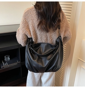 Détail du sac hobo en cuir noir grainé avec large bandoulière porté par un mannequin