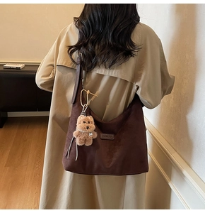 Detail of dark brown suede hobo bag with BANATU logo and plush bear charm on strap