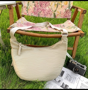 Detail of oat beige crescent crossbody bag with braided zipper on outdoor chair