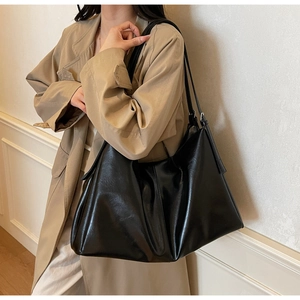 Detail of a black leather hobo shoulder bag with thin straps and hanging tassel decor