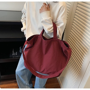 Detail shot of large red plaid canvas tote bag worn by model in cozy indoor setting