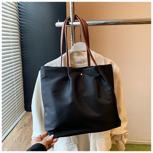 Detail of black nylon tote bag with brown leather handles and golden button closure