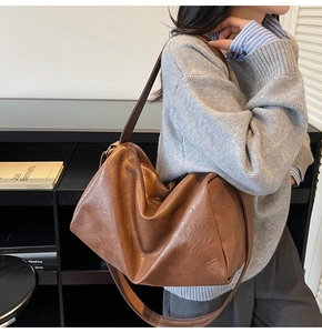 Brown soft leather hobo tote bag shown on shoulder in a minimalist room setting