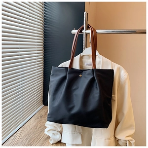 Close-up of black nylon tote bag with golden button and brown leather handles